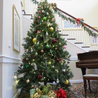 A beautifully decorated Christmas tree stands near a staircase, adorned with colorful ornaments and surrounded by festive decorations.