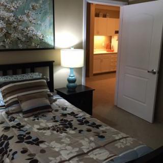 A cozy bedroom with a bed adorned with patterned bedding, a lamp on the bedside table, and an open door leading to a lit hallway.