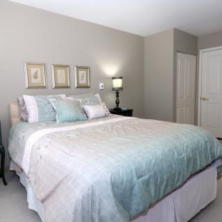 A cozy and well-decorated bedroom featuring a bed with pastel bedding, bedside lamp, and framed artwork on the wall.