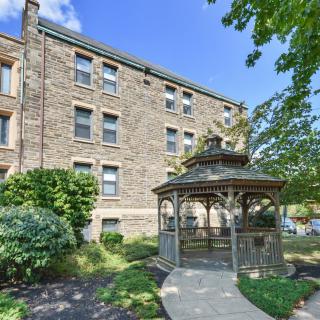 A brick apartment building with an adjacent wooden gazebo surrounded by greenery.