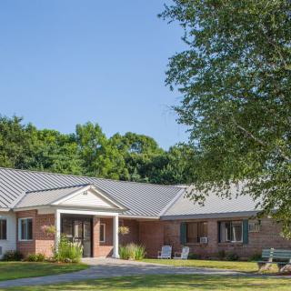 A single-story brick house with a well-maintained front yard and trees under a clear blue sky.