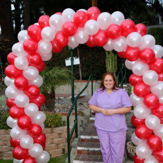 A person standing under a red and white balloon arch outdoors.