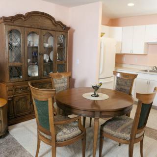 A cozy dining area with a wooden table, chairs, and a cabinet, adjacent to a kitchen.