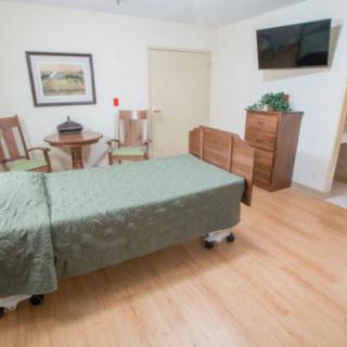 A simple bedroom with a single bed, television, and wooden furniture.