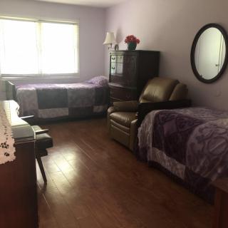 A cozy bedroom with two beds, purple blankets, a dresser, and a recliner.