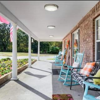 A cozy porch with rocking chairs and decorative pillows, next to a brick house and garden.