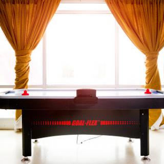 An air hockey table positioned in a well-lit game room, complemented by elegant curtains.