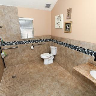 A spacious and accessible bathroom with tiled floors and walls, featuring a toilet, sink, and decorative elements.