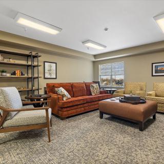 A cozy living room with a mix of sofas and armchairs, featuring a central coffee table and a bookshelf.