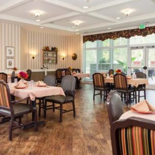 A cozy dining room with neatly arranged tables and chairs, decorated with floral centerpieces and natural lighting.