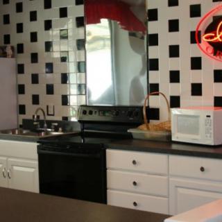 A retro-style kitchen with a black and white tiled wall, featuring a stove, microwave, and countertop space.