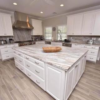 A spacious modern kitchen featuring white cabinets, a marble countertop island, and stainless steel appliances.