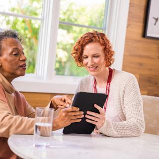 Two women engaging with a tablet at a cozy cafe, sharing knowledge and laughter.