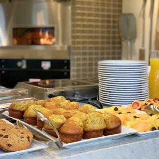 A breakfast buffet featuring muffins, cookies, fresh fruit, and orange juice.