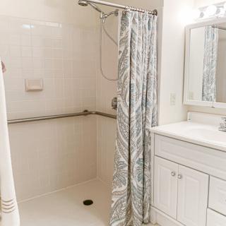 A clean and modern bathroom with a shower, curtain, and vanity mirror.