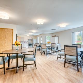 A modern dining area with several tables and chairs, featuring bright lighting and large windows.