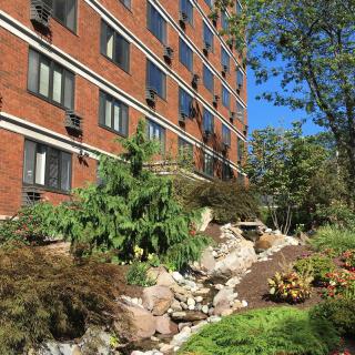 A red-brick building with manicured landscaping and various plants and trees on a sunny day.