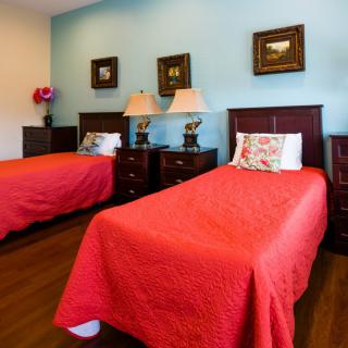 A cozy bedroom featuring twin beds with red bedding, complemented by wooden nightstands and elegant lamps.