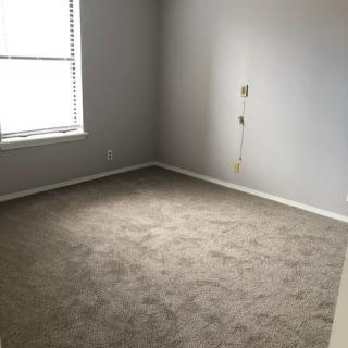 An empty room with a carpeted floor, a window, and neutral-colored walls.