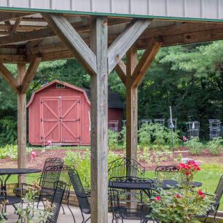 A peaceful garden setting with outdoor seating under a pergola, featuring a red barn in the background.