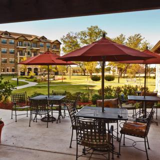 A serene outdoor patio area with tables and umbrellas overlooking a lush garden and building in the background.