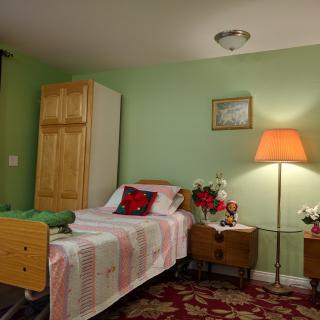A cozy bedroom featuring a hospital bed, wooden furniture, a lamp, and decorative elements such as a vase with flowers.