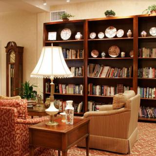 A cozy library living room with bookshelves, armchairs, and a grandfather clock.