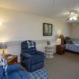 A cozy living space featuring armchairs, a bed, soft lighting, and decorative elements.