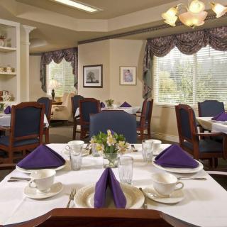 A well-decorated dining room with elegantly set tables featuring purple napkins and a chandelier overhead.