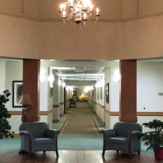 A well-lit lobby area featuring two chairs and a chandelier, leading into a long hallway.