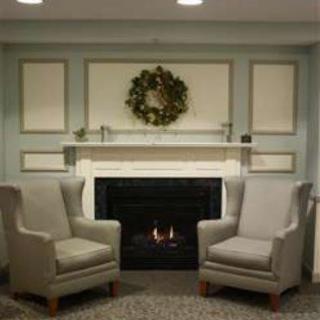 A cozy living room setup with two armchairs facing a lit fireplace, adorned with a wreath above.