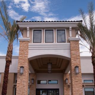 A modern architectural entrance framed by palm trees under a partly cloudy sky.