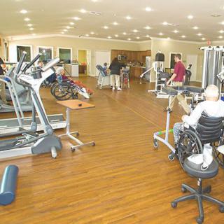 A rehabilitation gym with various exercise equipment and individuals engaging in physical therapy.