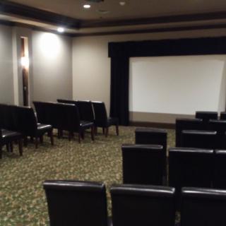 An empty theater room with rows of seats facing a projection screen.