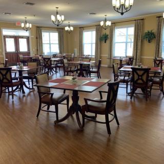 A spacious dining room with neatly arranged tables and chairs, featuring chandeliers and hardwood flooring.