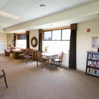 A cozy lounge area with seating, tables, and a bookshelf near large windows.