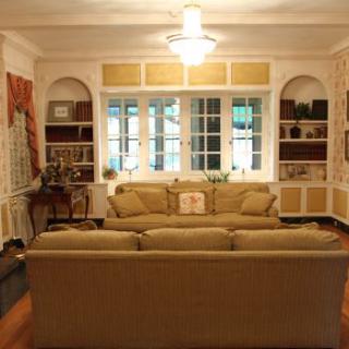 A cozy living room with a central sofa, flanked by built-in bookshelves and a large window.