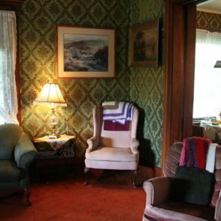A cozy vintage living room with patterned wallpaper, an armchair, and a warm lamp.