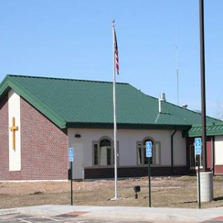 A modern church building featuring a green roof and a prominent cross.