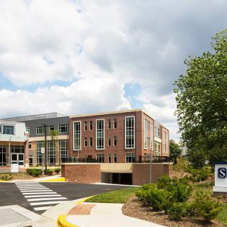 A modern school building surrounded by greenery under a cloudy sky.