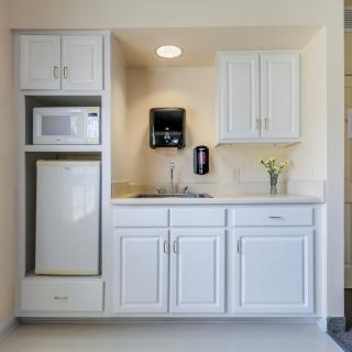 A minimalist kitchenette featuring white cabinets, a microwave, and a mini fridge.
