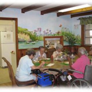 A group of seniors engaged in an activity around a table, with a colorful mural on the wall in the background.