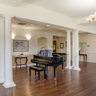 A spacious living area with a grand piano, hardwood floors, and classical columns.