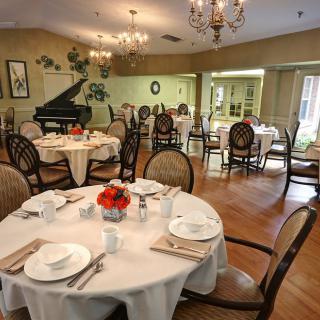 An elegant dining room with beautifully set tables, a grand piano, and charming chandeliers.