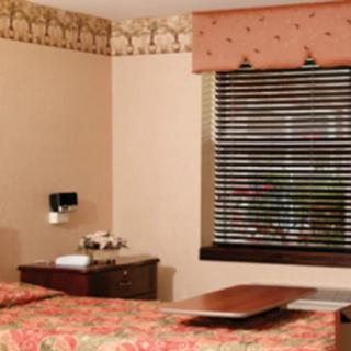 A cozy hotel room with a bed, bedside table, and window with blinds.