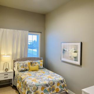 A cozy bedroom with a floral bedspread, bedside table with a lamp, and a picture on the wall.