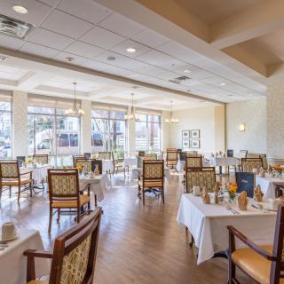 A spacious dining room with neatly arranged tables and chairs, featuring large windows that allow natural light to fill the space.