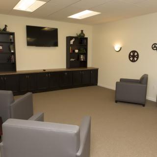 A modern lounge area featuring comfortable chairs, a wall-mounted television, and sleek shelving.
