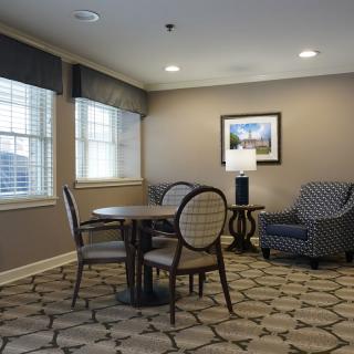A cozy living room area with a round table, chairs, an armchair, and a lamp beside framed artwork.
