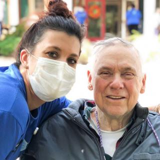 A nurse wearing a mask poses with an elderly patient outdoors.